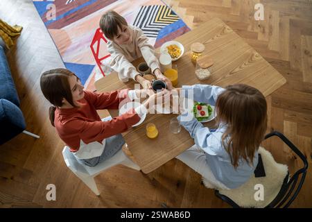 Famiglia felice di tre madri e due bambini che tengono una tazza di tè mentre mangiano la colazione insieme Foto Stock