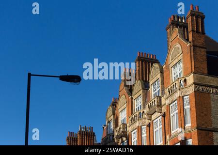 Edificio di epoca vittoriana, probabilmente a Londra, caratterizzato da mattoni ornati e camini multipli. Un lampione stradale è visibile contro un cielo azzurro. Foto Stock