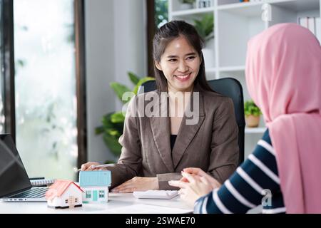 Agenti immobiliari diversi sorridono mentre discutono di più case modello con il cliente in un ambiente ufficio luminoso. Foto Stock