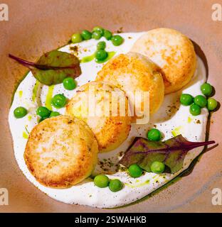 Frittelle di formaggio cottage adagiate su salsa bianca e decorate con piselli verdi e foglie di barbabietola Foto Stock