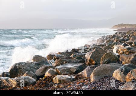 L'oceano è ruvido e le rocce sono grandi. Le onde si schiantano contro le rocce, creando una scena potente e dinamica. La scena e' una di forza Foto Stock