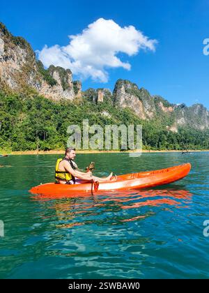 Avventuriero in kayak in un vivace kayak arancione su un lago tranquillo circondato da maestose montagne Foto Stock
