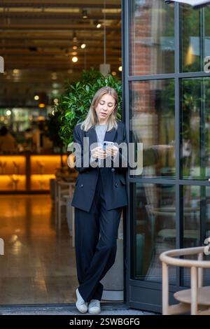 Donna concentrata proprietaria di un bar moderno che utilizza un messaggio di digitazione telefonica, esamina le proposte di sviluppo aziendale. Foto Stock
