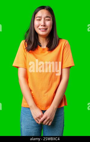 Giovane donna in camicia arancione che esprime tristezza su sfondo verde durante il momento emotivo Foto Stock