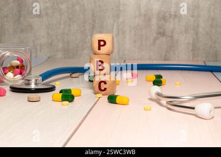PBC colangite biliare primaria - parola da blocchi di legno con lettere su sfondo bianco circondate da pillole colorate. Concetto medico. Foto Stock