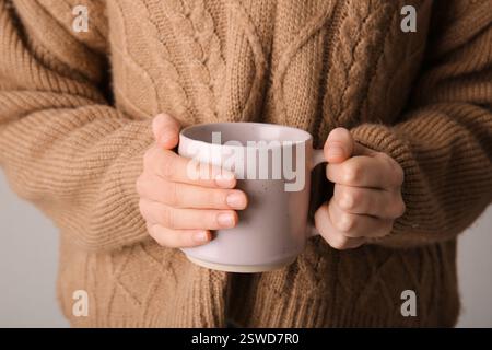 Donna in un elegante pullover lavorato a maglia con tazza in ceramica, primo piano Foto Stock