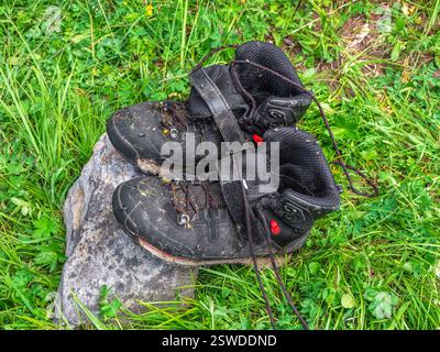 Scarponi neri bagnati asciutti su una pietra sullo sfondo dell'erba verde. Difficoltà di trekking, asciugare vestiti in natura. Foto Stock