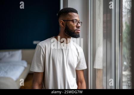 Triste uomo nero guardando fuori dalla finestra pensando a problemi di vita, affrontando la depressione di rottura Foto Stock
