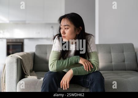 Donna asiatica triste e solitaria che ha sintomi di depressione preoccupandosi di soldi o problemi familiari Foto Stock