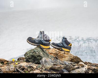 Scarponi da trekking bagnati asciutti su una pietra sullo sfondo di alte montagne innevate. Le difficoltà dell'escursionismo, dell'asciugatura del mantello Foto Stock