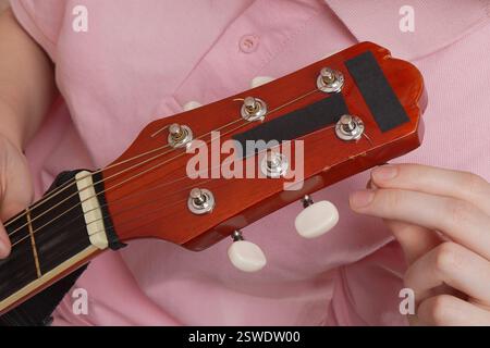 Primo piano estremo delle dita della donna mentre sintonizza la chitarra acustica spagnola a sei corde. Procedura quotidiana di serraggio e allentamento delle stringhe Foto Stock