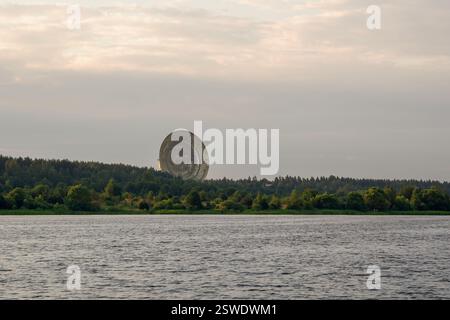 Un'enorme parabola satellitare sopra la foresta sulla riva del fiume. Foto Stock