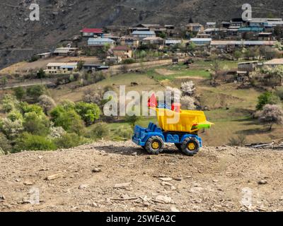 Camioncino sporco giallo giocattolo sullo sfondo di un paesaggio montano. Foto Stock