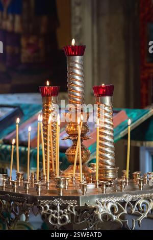 Le candele della chiesa bruciano su un grande candelabro d'epoca dorato nella chiesa ortodossa. Fede e tradizioni cristiane. Tema o Foto Stock