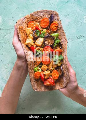 Pezzi di filetto di curry di pollo fritto su pane di segale con verdure. Tortilla con verdure e carne alla griglia in mano Foto Stock