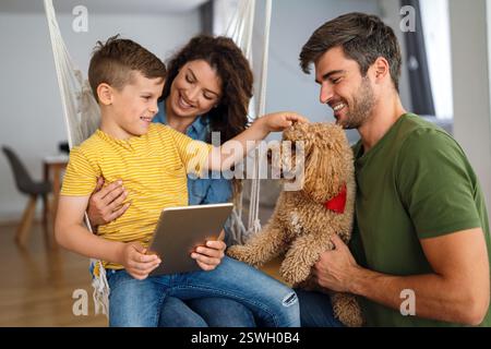Famiglia felice con un bambino che si diverte a usare il tablet insieme, genitori e bambini che ridono rilassandosi a casa Foto Stock