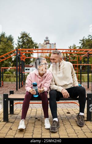 Una coppia amorevole condivide le risate mentre si siede su una panchina in un parco, godendosi la compagnia degli altri. Foto Stock
