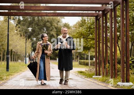 Un paio cammina di mano in mano in un parco, gustando bevande calde e sorrisi. Foto Stock