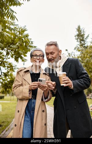 Una coppia amorevole cammina mano nella mano, condividendo sorrisi e risate mentre controllano il loro smartphone. Foto Stock