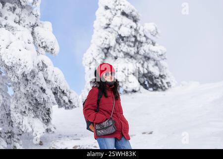 Donna adulta in piedi di fronte a pini innevati sulla collina Foto Stock