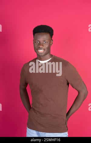Un uomo con una camicia marrone e capelli neri sorride per la macchina fotografica. L'immagine ha un'atmosfera calda e amichevole, con il sorriso dell'uomo e la ba rosa brillante Foto Stock