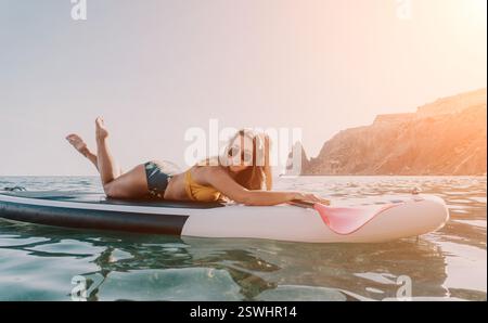 Donna Paddleboard Ocean - donna felice sdraiata sul paddleboard nell'oceano con pagaia in mano. Foto Stock