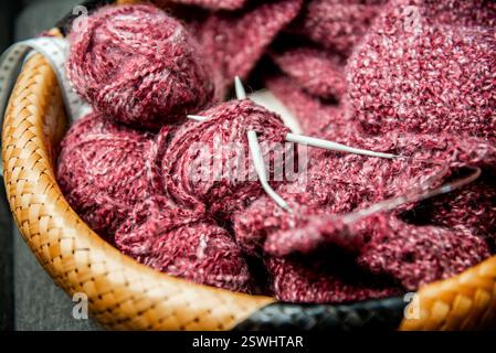 yarns, knitting needles and pattern sample in basket on sofa. closeup Foto Stock