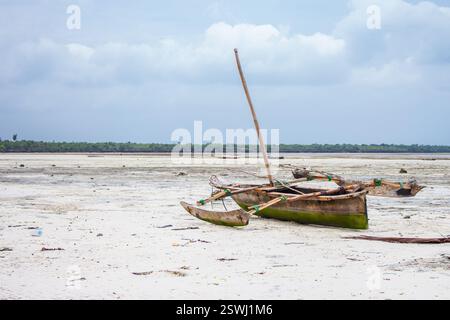 Banka in legno arrugginito ancorata alla spiaggia. Paesaggio tropicale con bassa marea con barche a vela. Nave nautica vicino alla costa delle palme, Africa, Zanzibar. Foto Stock