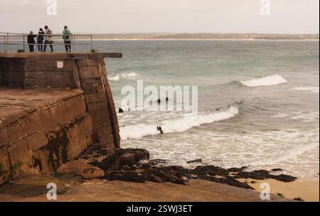 I vacanzieri si trovano alla fine di New Pier St Ives, Cornovaglia, Inghilterra, Regno Unito, e si affacciano sul mare e sulle onde del mare Foto Stock