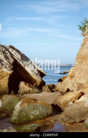 Grandi rocce costiere frastagliate contro l'orizzonte blu profondo dell'oceano sotto un cielo limpido e soleggiato. Foto Stock