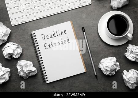 Scadenza testo esteso in notebook, matita, caffè, tastiera del computer e palle di carta increspate su tavolo nero, disposizione piatta Foto Stock