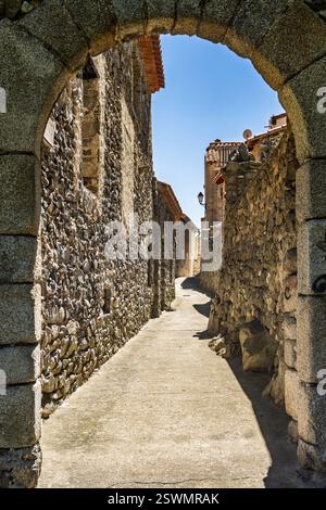 Arco in pietra che conduce a una stretta strada storica a Mosset, in Francia, sotto il cielo blu. Foto Stock