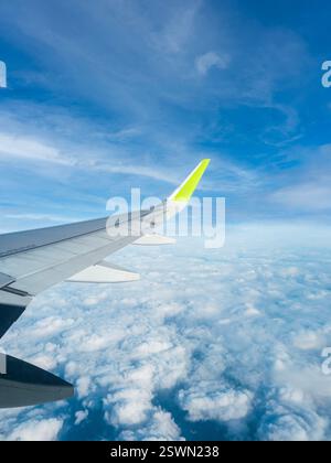 Vista dall'ala di un aeroplano sopra le soffici nuvole su un cielo blu luminoso durante un volo alla luce del giorno Foto Stock