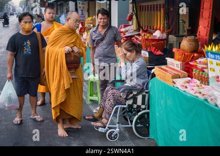Un monaco buddista tailandese nella sua mattinata di elemosina, accolto con un Wai (tradizionale saluto tailandese) da una laica in una strada a Bangkok, Thailandia Foto Stock
