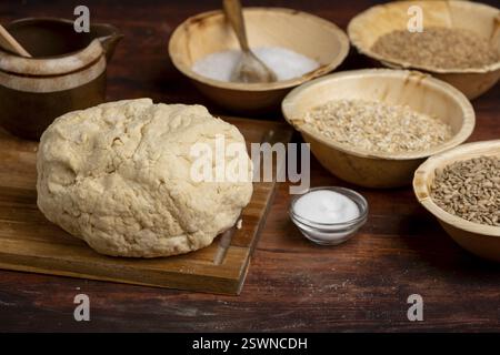 Un pezzo di impasto e vari grani e sale in ciotole di legno su un tavolo di legno Foto Stock