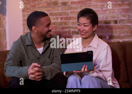 Colleghi che condividono idee e lavorano al progetto utilizzando un tablet in un ufficio loft Foto Stock