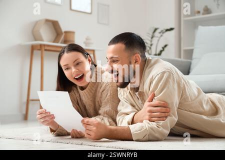 Felice giovane coppia con modulo di rimborso sdraiato sul pavimento di casa Foto Stock
