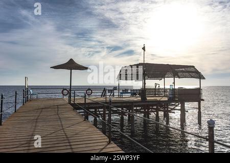 Lungo molo in legno si estende nelle tranquille acque di marsa Alam, egitto, sotto un sole luminoso e un bel cielo nuvoloso Foto Stock