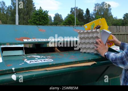 Värmland, Svezia. Gettare la carta nel contenitore di riciclaggio verde all'esterno. Solo mani e braccia mostrate. Concetto di cambiamento climatico. Foto Stock