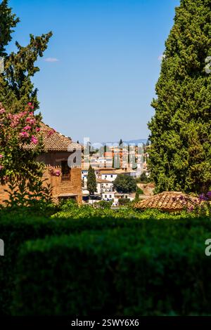 Una pittoresca veduta di Granada incorniciata dai giardini verdeggianti dell'Alhambra e dall'architettura storica, che si affaccia sulle case bianche e sugli alberi di cipresso Foto Stock