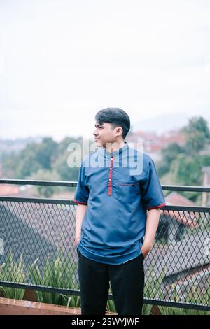 Un giovane con un kurta blu guarda con attenzione il panorama circostante. La scena è tranquilla e tranquilla, invitando lo spettatore a condividere il mese Foto Stock