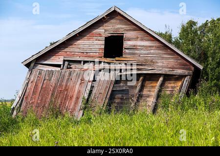 Fienile con un tetto rotto e una finestra. Il fienile è in un campo. Il tetto è inclinato lateralmente Foto Stock