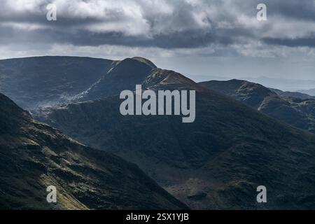 Lussureggianti montagne verdi si estendono lungo l'orizzonte, avvolte da ombre e illuminate da luce soffusa, con nuvole scure che aggiungono una profondità d'atmosfera a questo Foto Stock