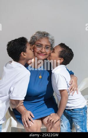Due nipoti stanno baciando la nonna sulle guance, mostrando il loro amore e affetto Foto Stock