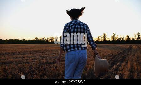 Contadina che corre attraverso la piantagione di orzo al tramonto. L'agronomo fa jogging tra i prati di grano al crepuscolo. Splendido paesaggio panoramico. Concetto di Foto Stock