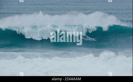 Surfista solitario sulle enormi onde dell'oceano Atlantico durante la sfida internazionale dei surfisti a Praia do Norte a Nazare, Farol da Nazaré, Portogallo, dove Guinness Foto Stock