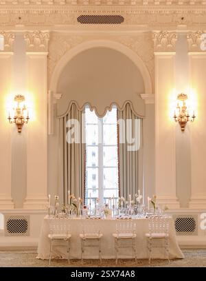 Un tavolo da pranzo elegantemente disposto e' allestito in una sofisticata sala caratterizzata da luci soffuse e decor decorato. Foto Stock