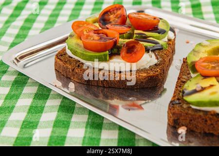 I panini a vista preparati al momento si trovano su un vassoio di metallo Fette di pane ricoperte di formaggio spalmabile, cetrioli e pomodori ciliegini poggiano su una scacchiera Foto Stock
