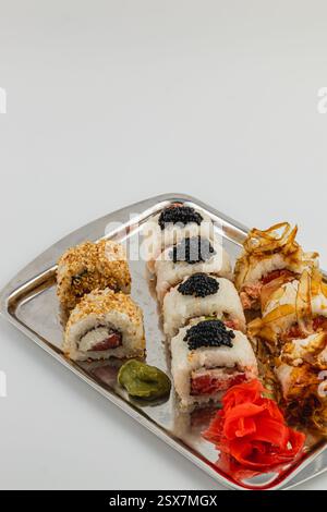 Un piatto di sushi presenta un assortimento di panini, tra cui varietà ricoperte di sesamo e ricoperte di caviale. Le decorazioni di accompagnamento includono wasabi e sottaceto Foto Stock