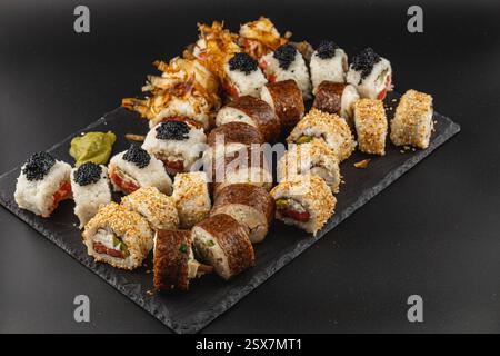 Un elegante piatto di sushi presenta una varietà di sushi roll splendidamente disposti su un vassoio nero Gli ingredienti freschi includono riso, pesce e garnishe Foto Stock